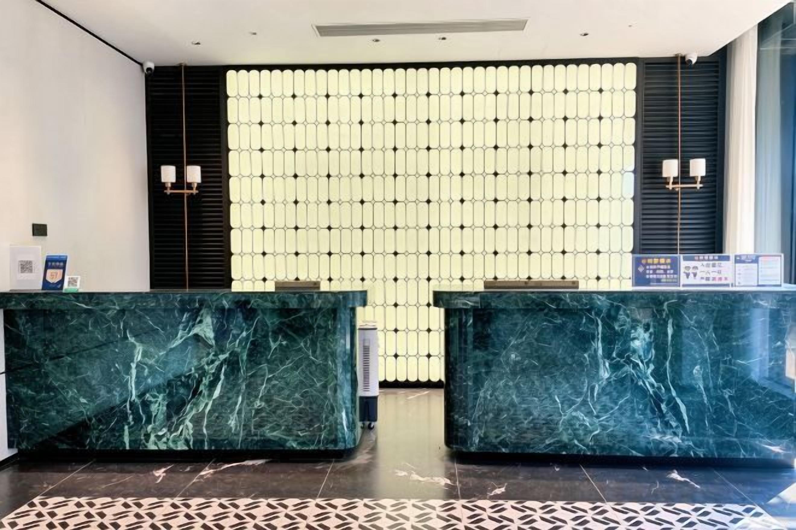 A reception area with marble reception desks, a patterned floor, and a wall of light fixtures.
