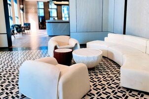 En moderne lobby med et geometrisk gulvmønster, hvide sofaer og et rundt træbord.