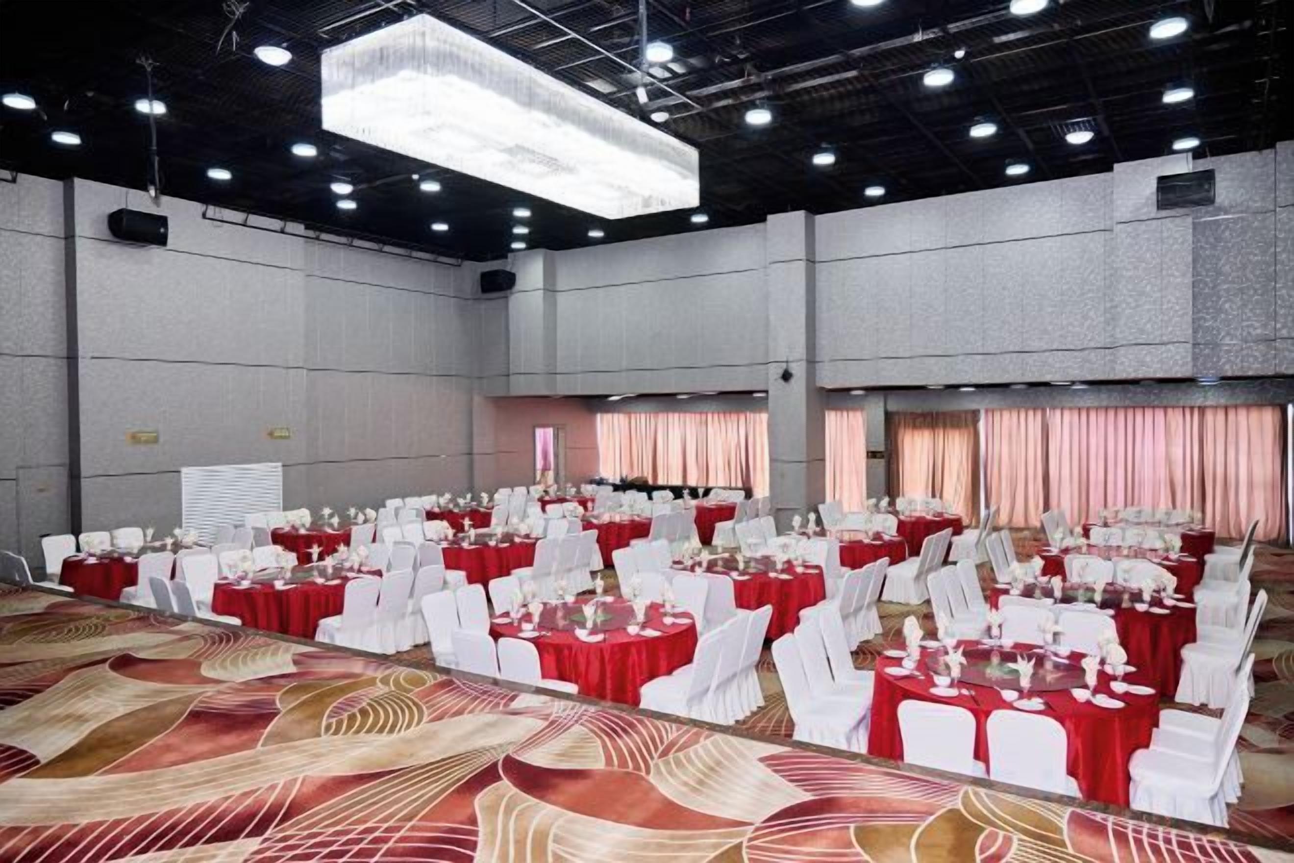 A large banquet hall with rows of tables and chairs, a patterned carpet, and a high ceiling with lighting fixtures.
