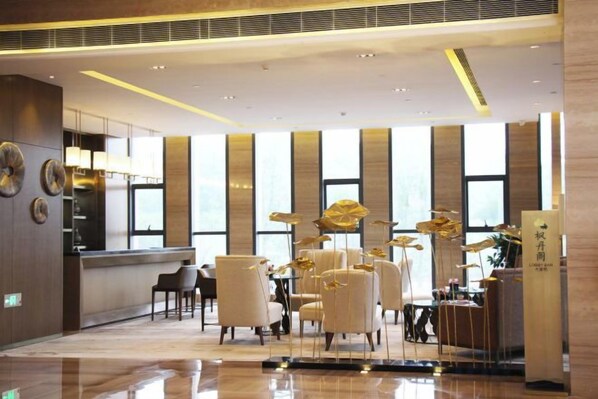 Un vestíbulo de hotel con mostrador de recepción, zona de estar y grandes ventanales.