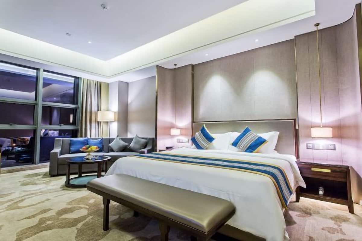 A modern hotel room with a large bed, a sofa, a bench, and a small table.
