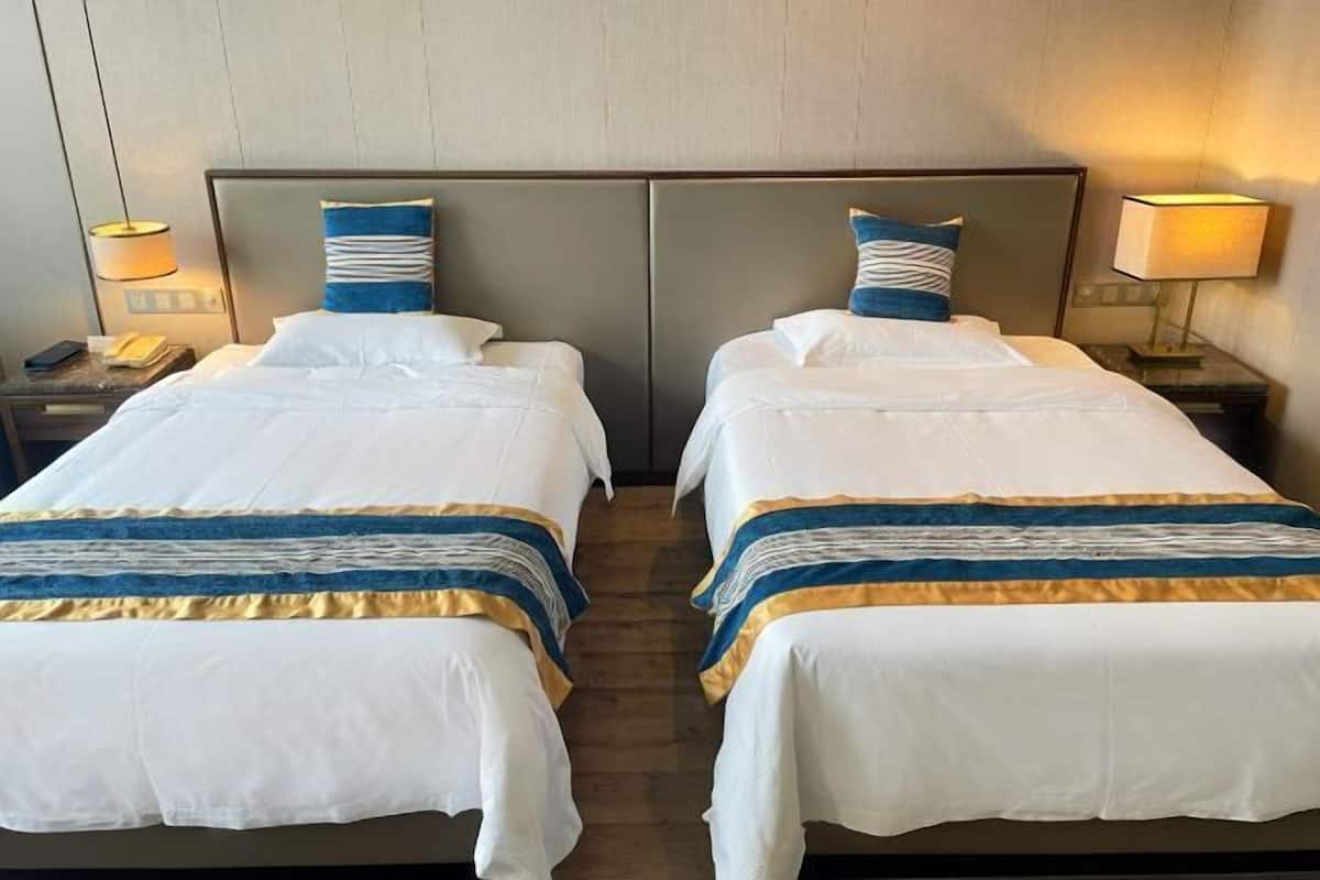 A hotel room with two beds, each with a headboard, bedside tables, and lamps.
