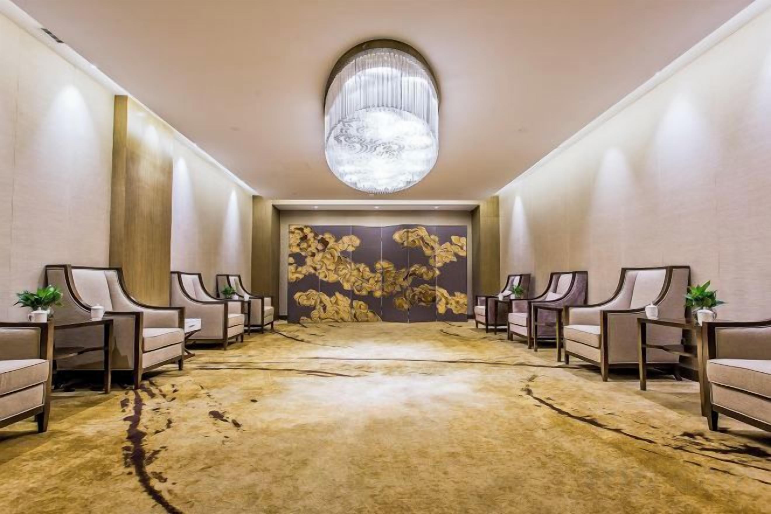 A hotel lobby with a large chandelier, a patterned wall, and a carpeted floor.