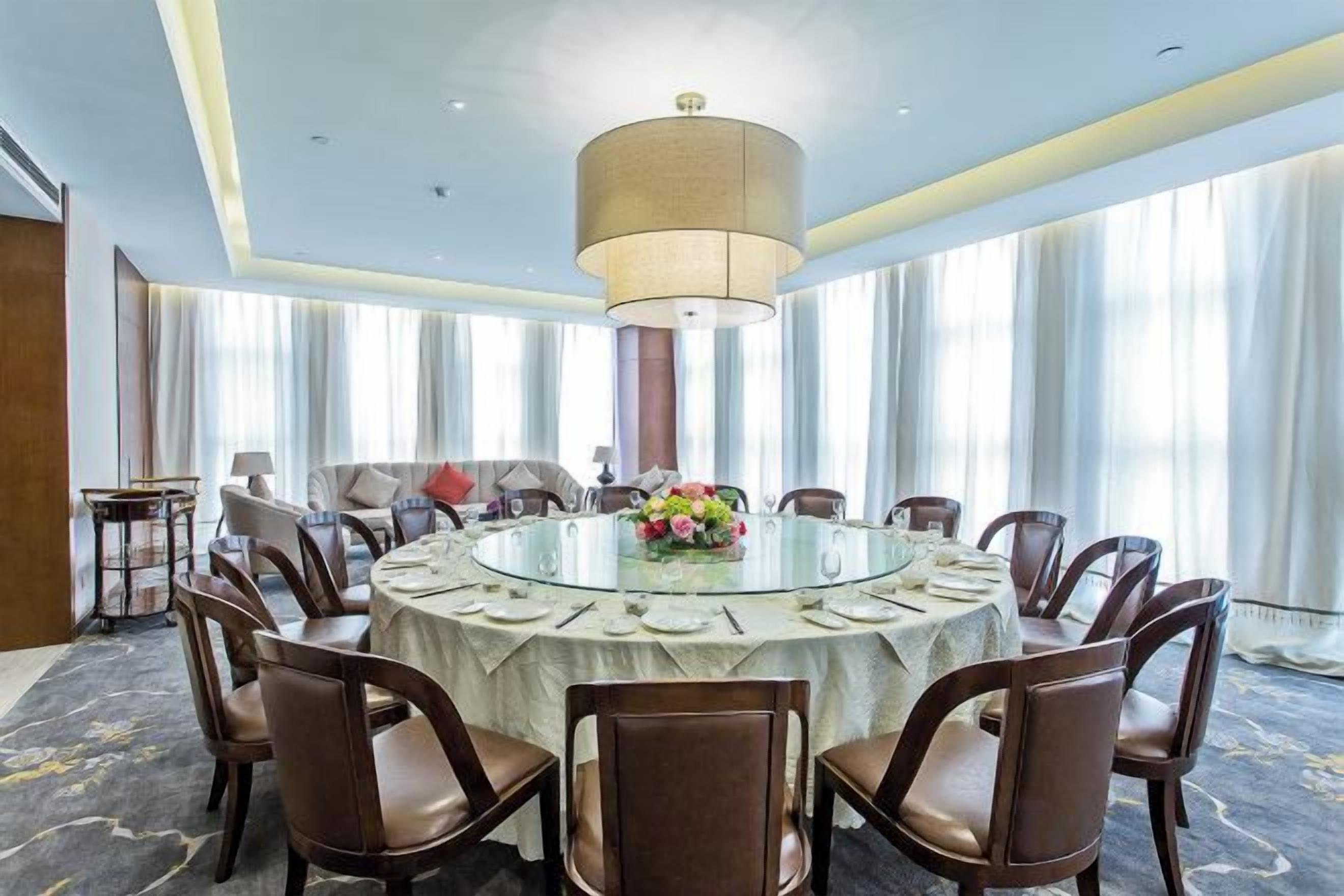 A conference room with a round table, chairs, a chandelier, and a large window with curtains.