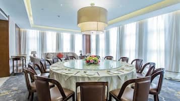 A conference room with a round table, chairs, a chandelier, and a large window with curtains.
