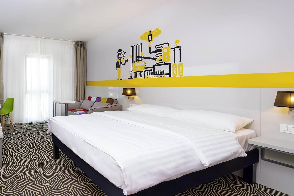 A hotel room with a bed, bedside tables, a desk, a chair, and a wall decoration.