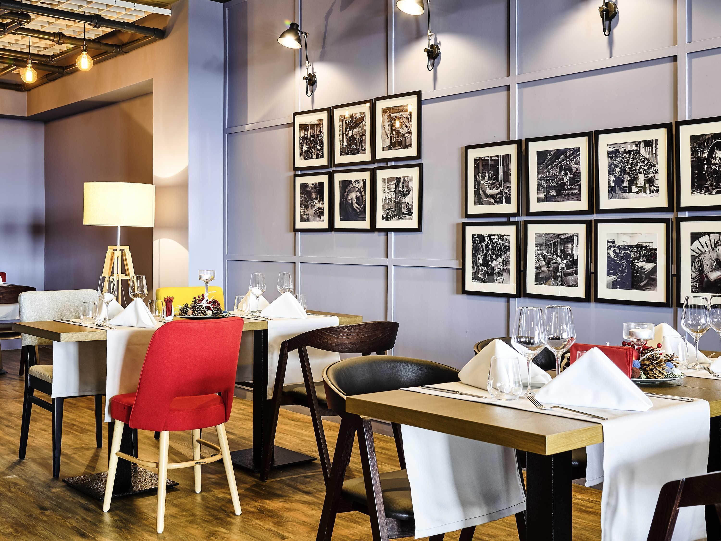 A restaurant interior with tables set for dining, framed black and white photographs on the wall, and a modern chandelier.