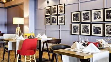 A restaurant interior with tables set for dining, framed black and white photographs on the wall, and a modern chandelier.