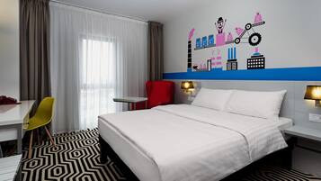 A hotel room with a bed, a desk, a chair, a wall with a cityscape mural, and a patterned floor.
