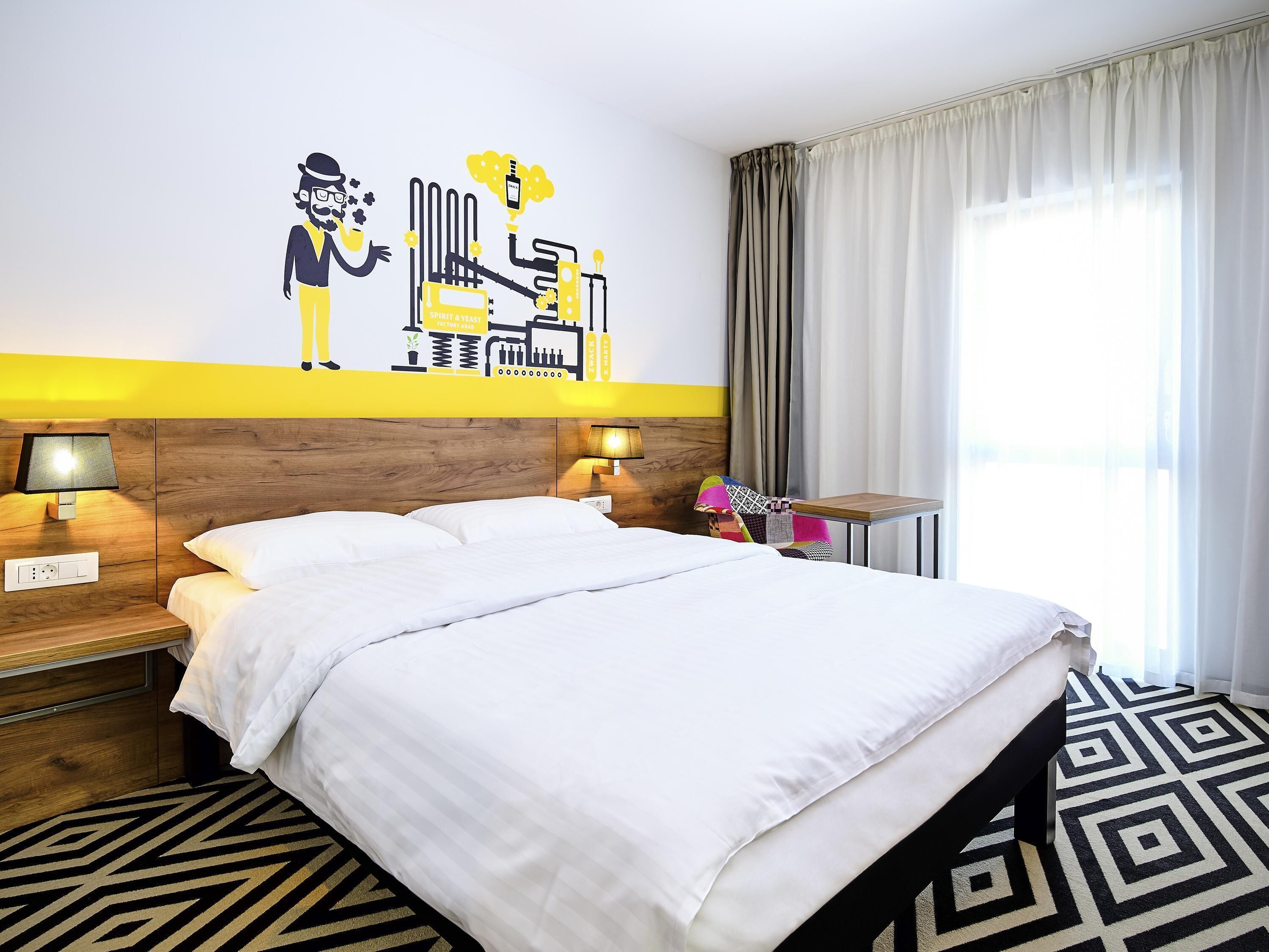 A hotel room with a large bed, two bedside tables with lamps, a wall mural, and a window with curtains.