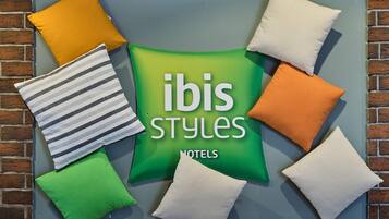 Eine Wand mit einem grünen Schild, auf dem 'ibis Styles' und 'Hotels' steht, umgeben von Kissen in verschiedenen Farben.