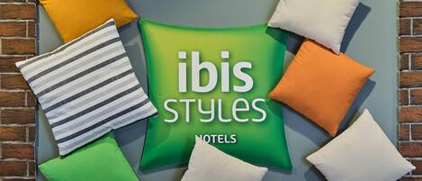 Una pared con un letrero verde que dice 'ibis styles' y 'hoteles', rodeada de almohadas de colores variados.