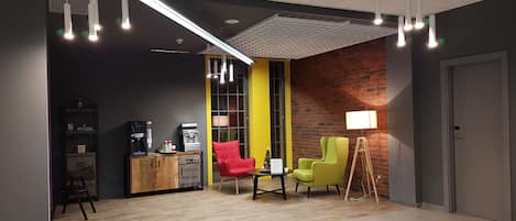 A modern office space with a wooden floor, a coffee machine, a red and a green chair, and a lamp.