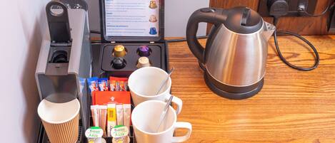 A breakfast setup with a coffee maker, tea maker, and a kettle on a tray, along with cups and milk containers.