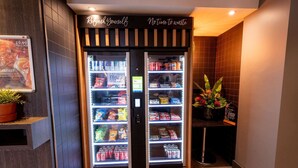 A vending machine with snacks and drinks, a sign above it, and a potted plant nearby.