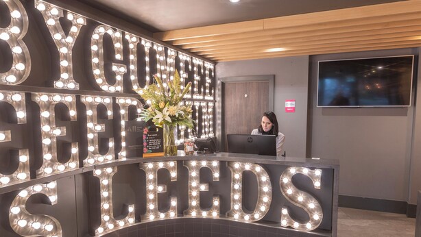 A reception desk with illuminated letters spelling "YOUR LEADS" and a receptionist behind it.