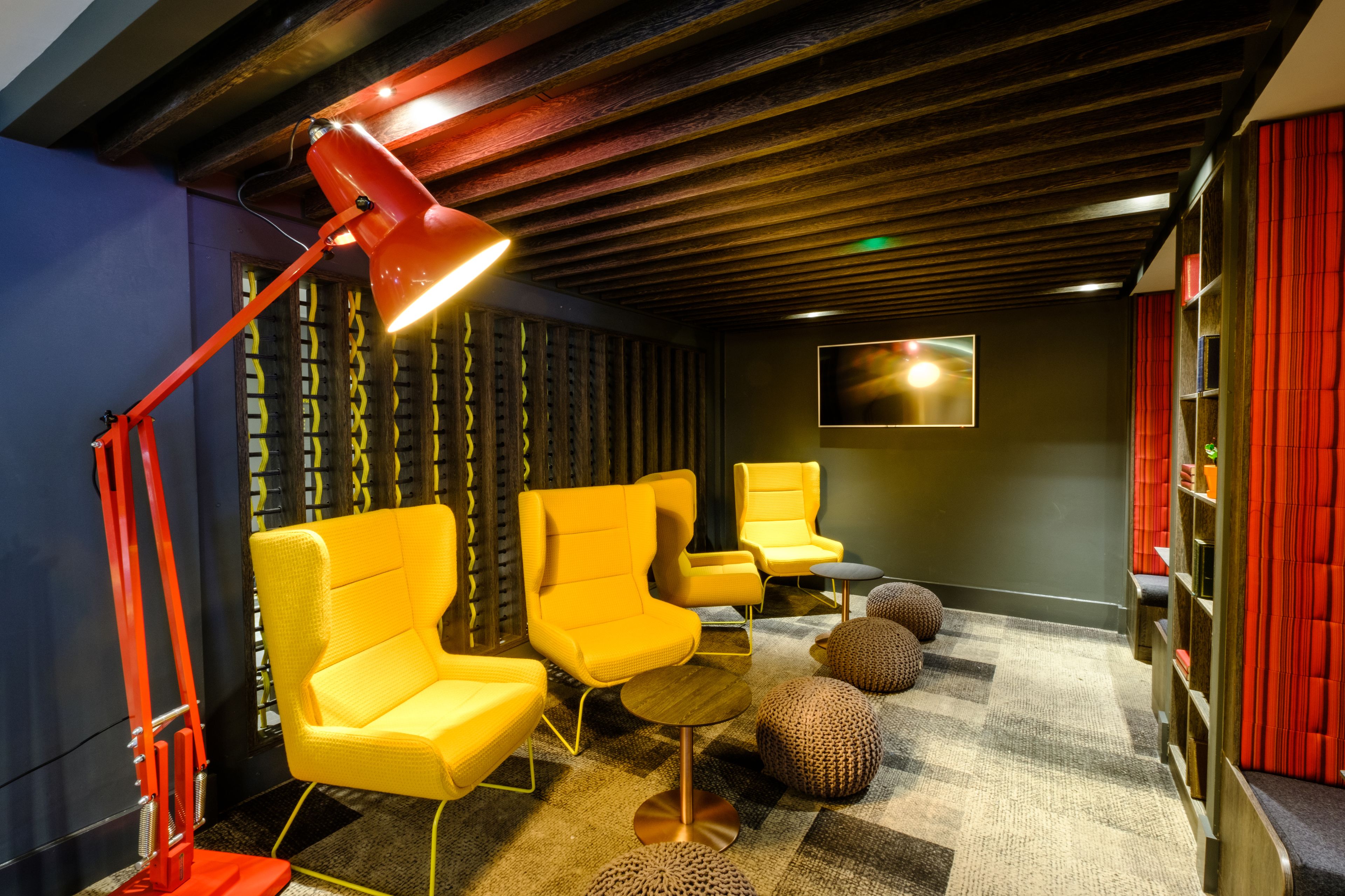 A modern lounge with yellow armchairs, a red floor lamp, and a checkered carpet.