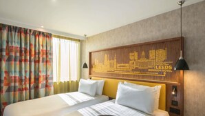 A hotel room with two beds, a city-themed headboard, a round table, and a small bedside table.