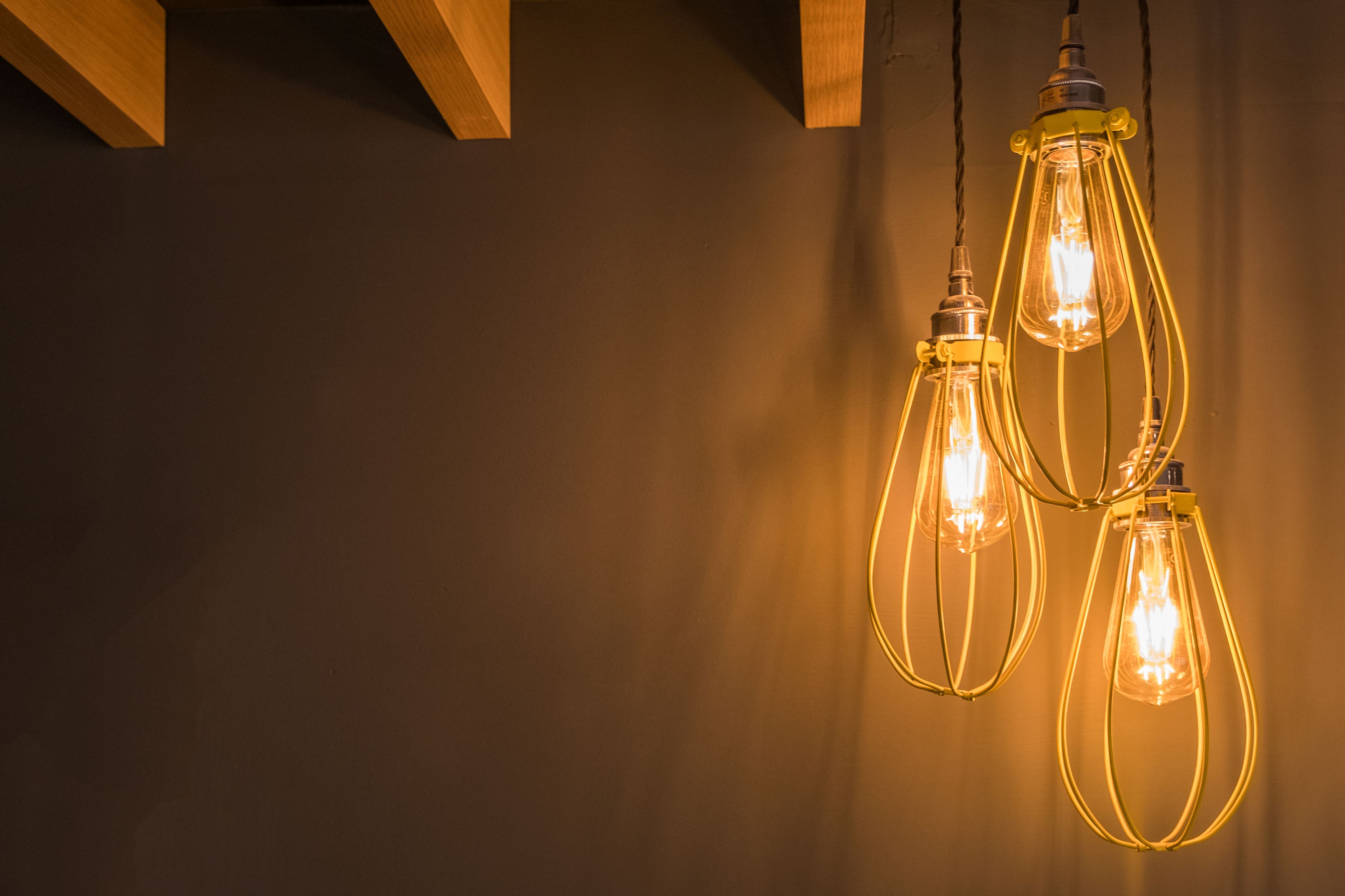 Three hanging light fixtures with exposed bulbs against a plain wall.