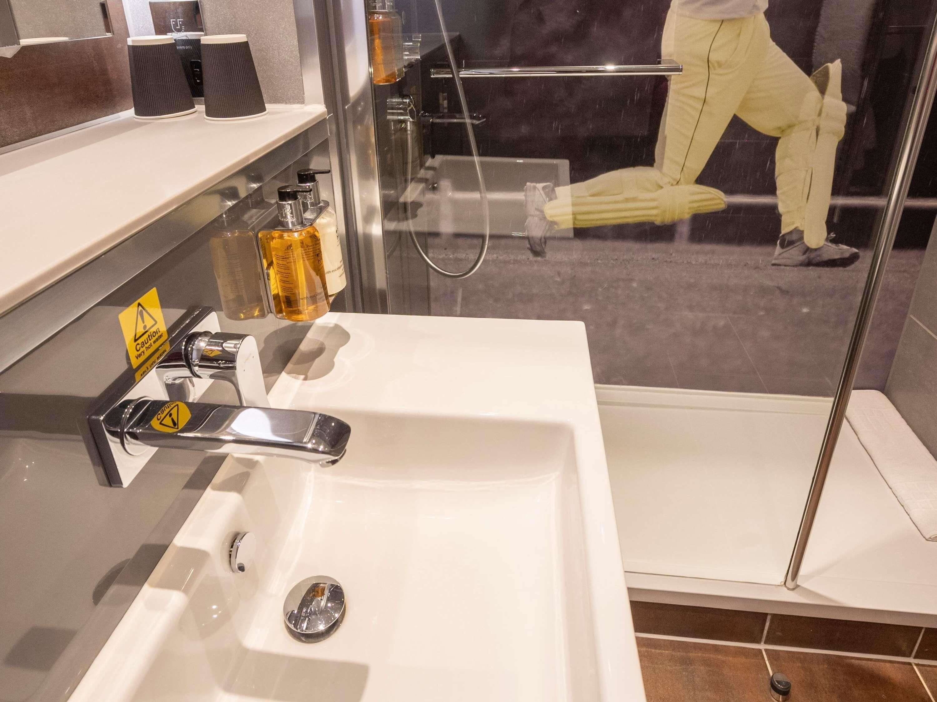 A modern bathroom with a white sink, a glass shower enclosure, and a shelf with toiletries.