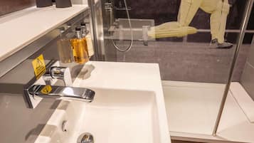 A modern bathroom with a white sink, a glass shower enclosure, and a shelf with toiletries.