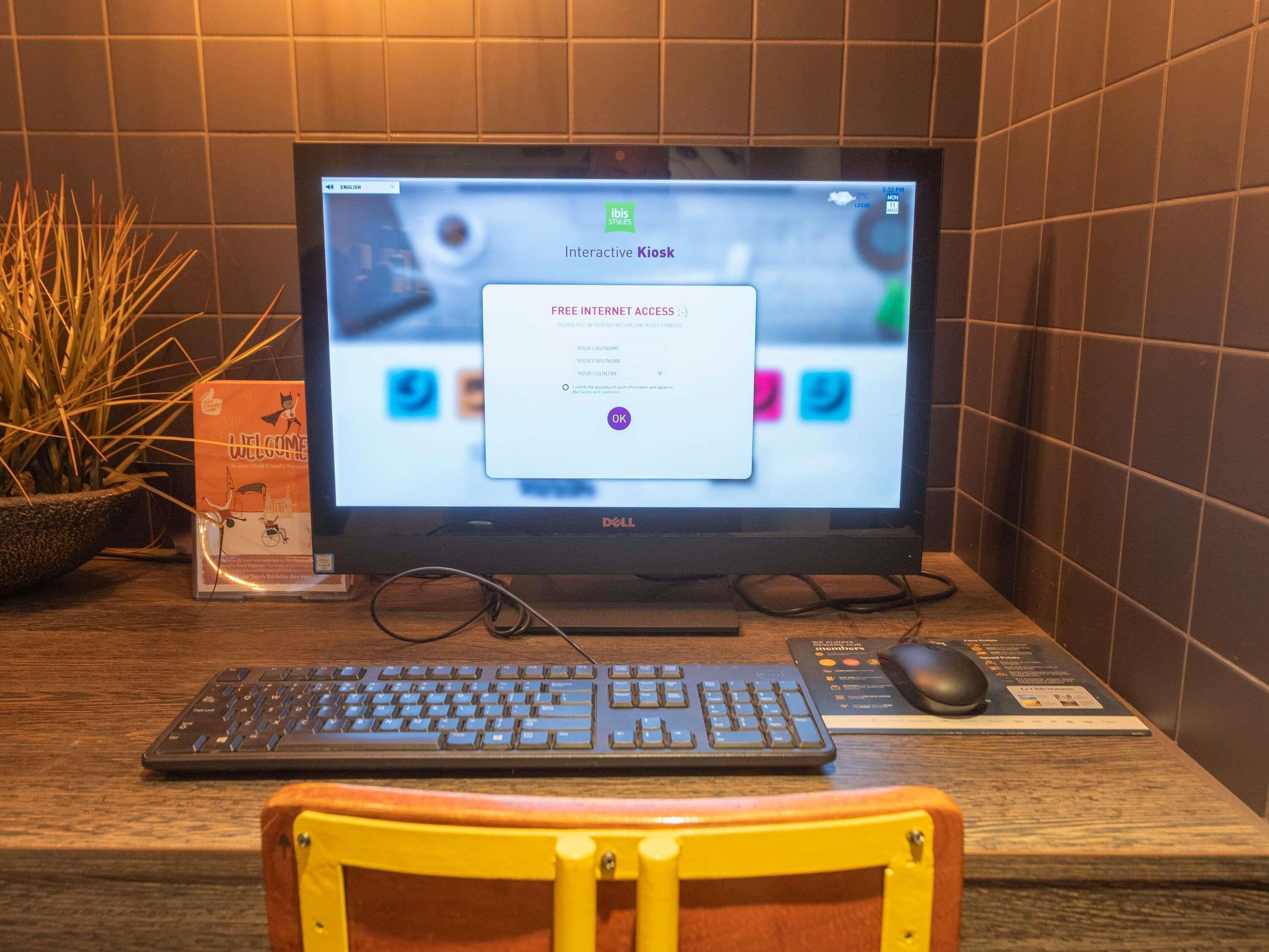 Ein Computerbildschirm auf einem Schreibtisch mit Tastatur und Maus, ein Schild mit dem Rollstuhlsymbol und einer Pflanze.