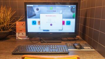 Monitor de computadora sobre un escritorio, con teclado, ratón y una planta. Se observa un cartel con el símbolo de una silla de ruedas.