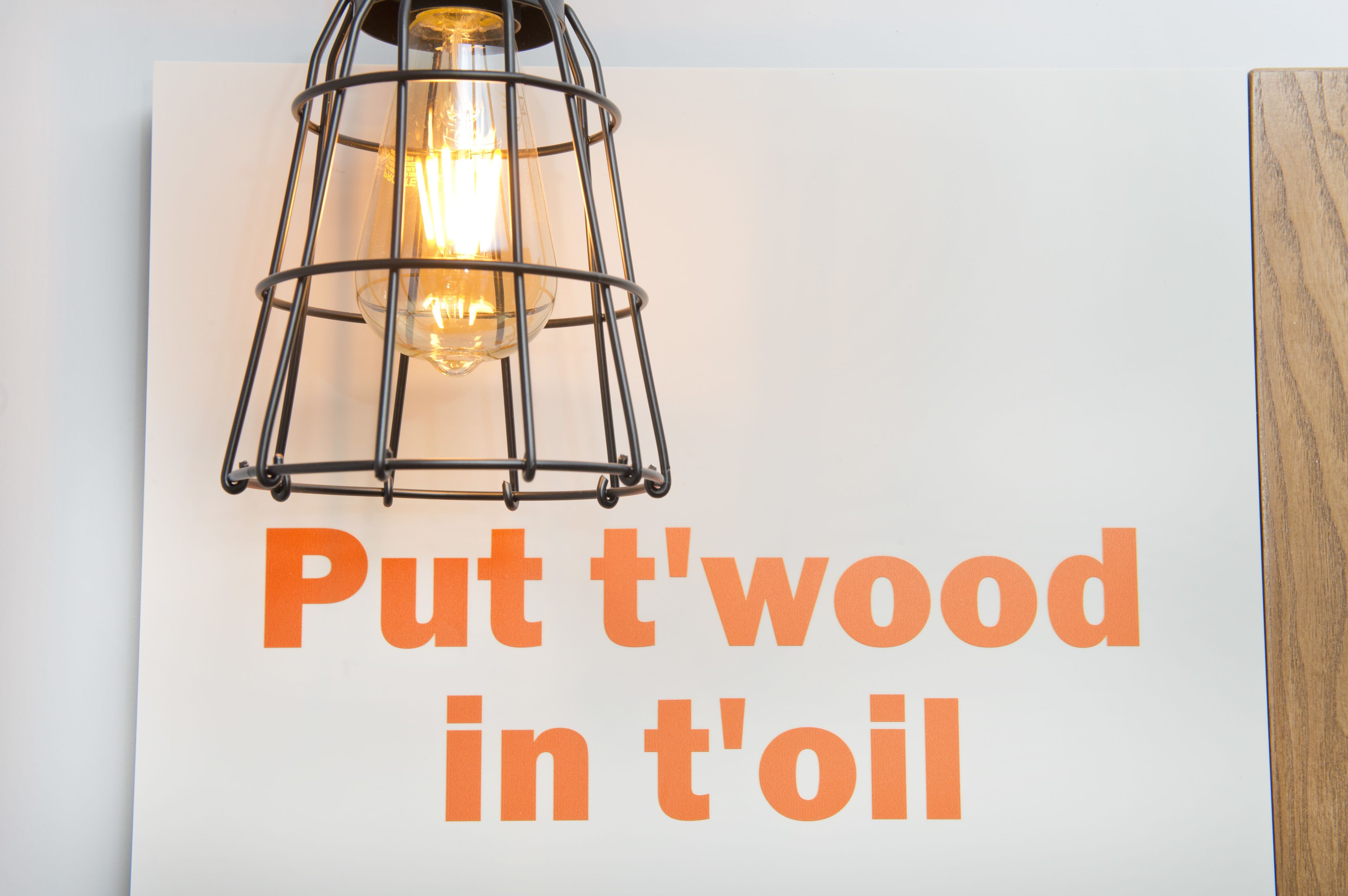A wall with a sign that reads "Put t'wood in t'oil" and a hanging light fixture.