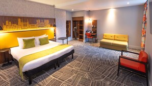 A hotel room with a large bed, a sofa, a chair, a desk, and a bookshelf.