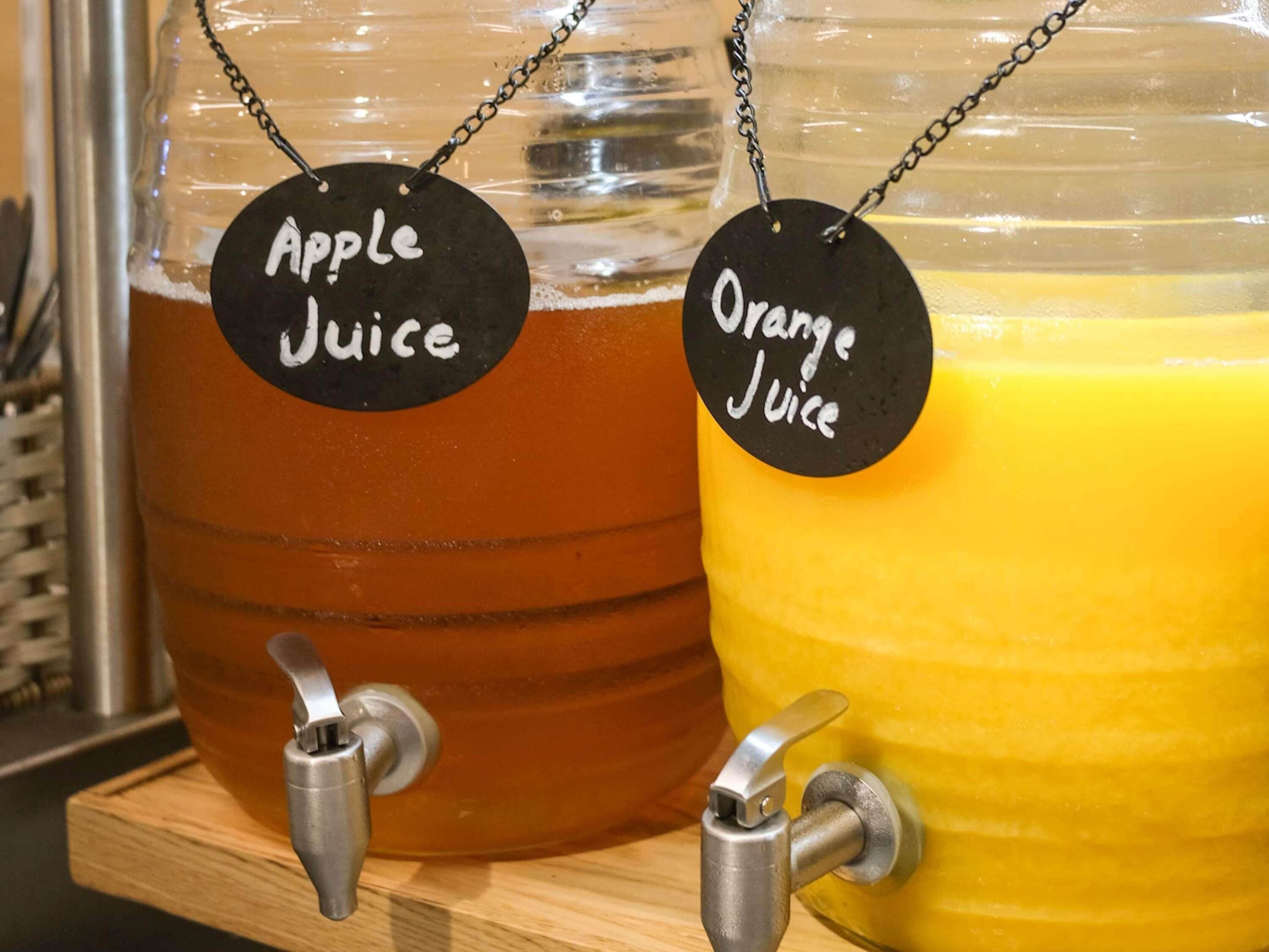 Zwei Getränkespender mit Beschriftung für Apfelsaft und Orangensaft.