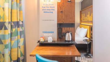 A hotel room with a wooden table, a blue chair, a kettle, and a tray with tea bags and a mug.