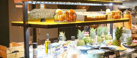 A buffet with various food items and beverages, including fruits, pastries, and condiments.