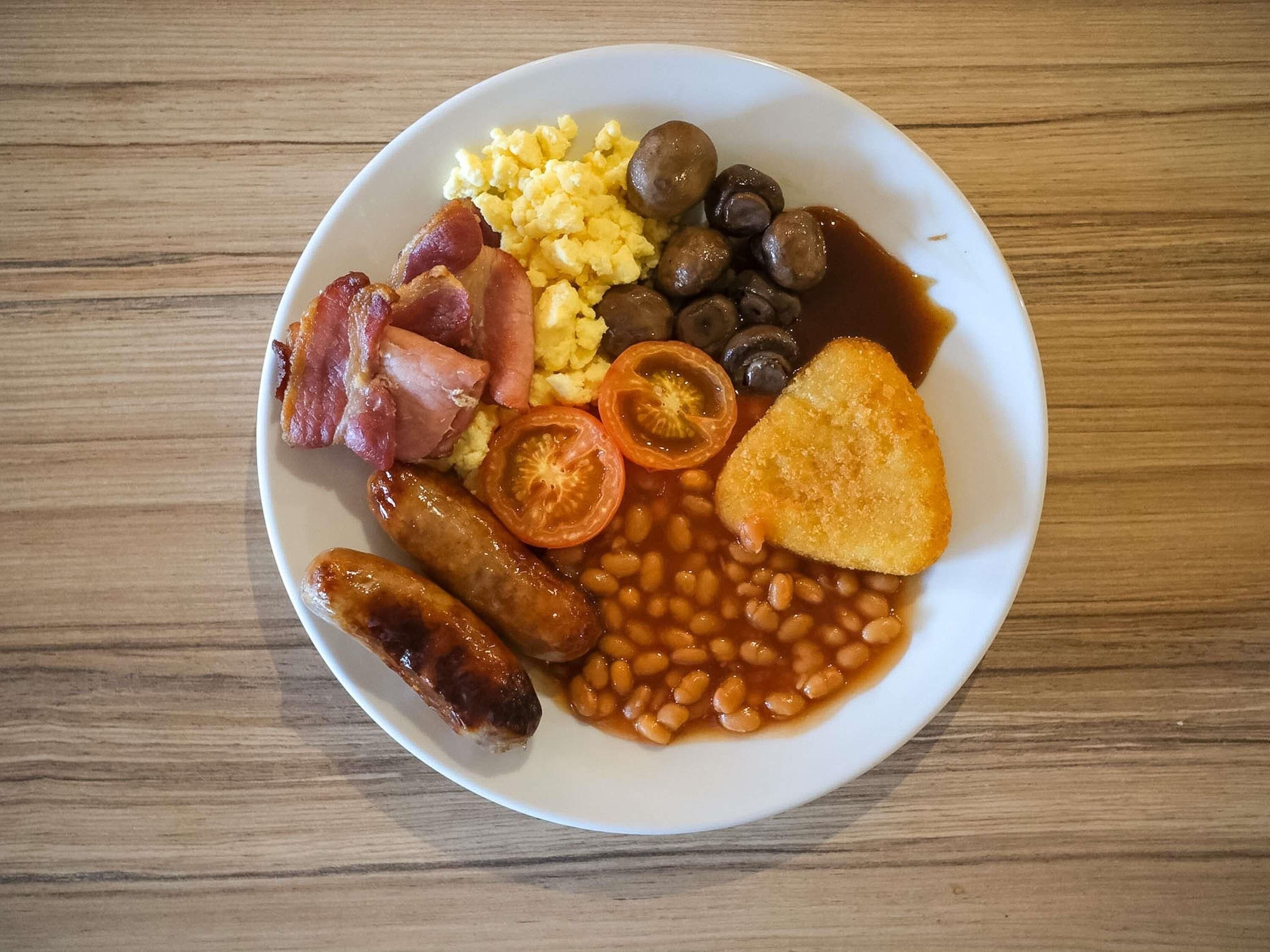 Une assiette de nourriture comprenant des saucisses, des haricots, des tomates et des tranches de pain grillé.