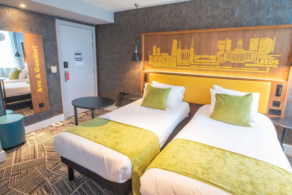 Habitación de hotel con dos camas, un cuadro con vista a la ciudad, una mesita redonda y una silla azul.