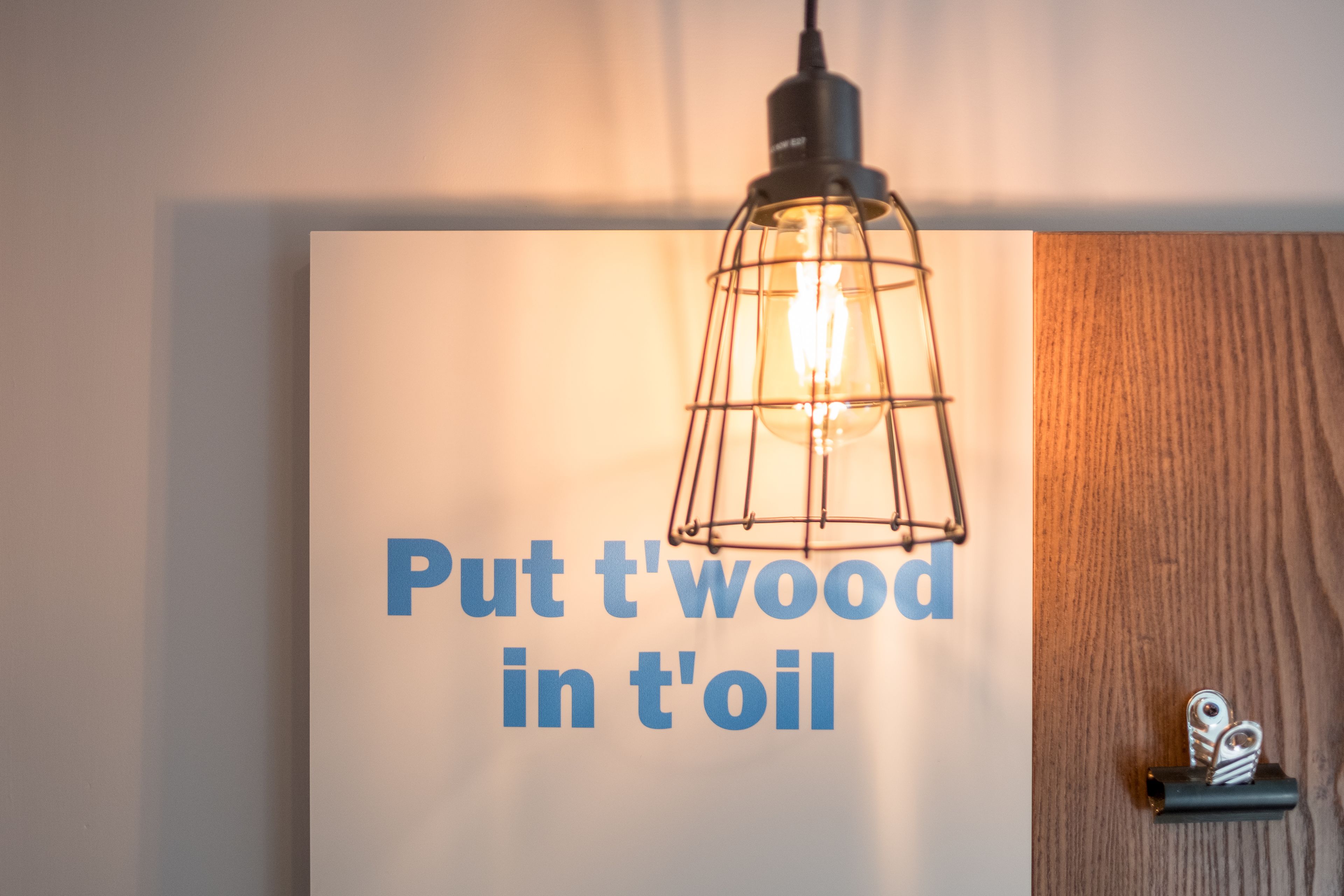 Un mur avec une enseigne affichant le texte « Put t'wood in t'oil » et un luminaire suspendu.