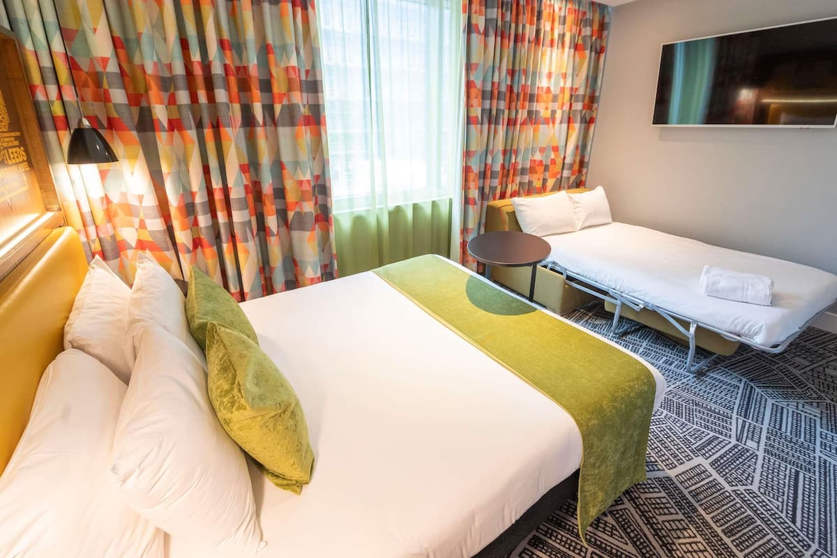 A hotel room with a bed, a sofa, a small table, and a TV.