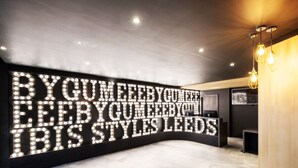 A modern interior with a large illuminated sign on the wall, a curved reception desk, and a wooden panel on the right.