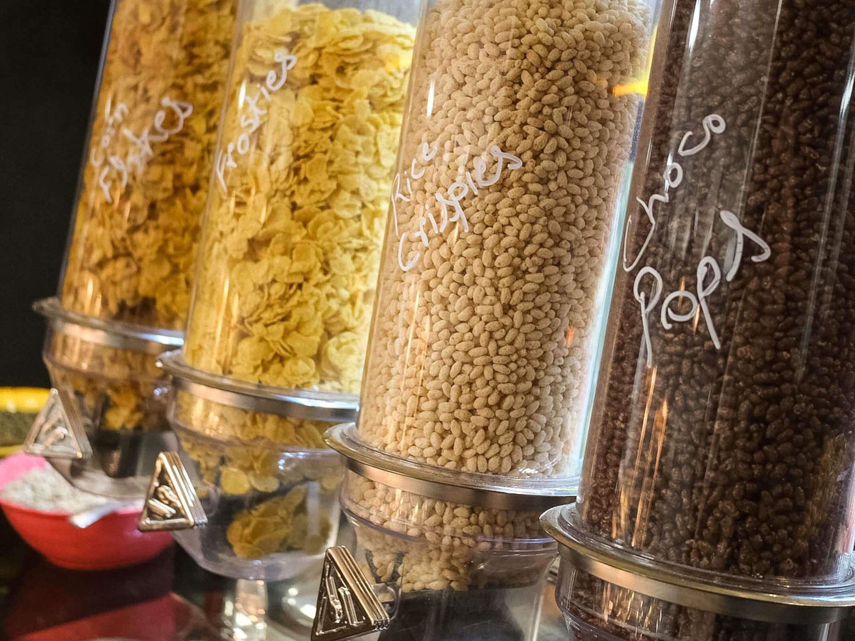 Varios recipientes de vidrio etiquetados con diferentes nombres de cereales, probablemente en una tienda o despensa.
