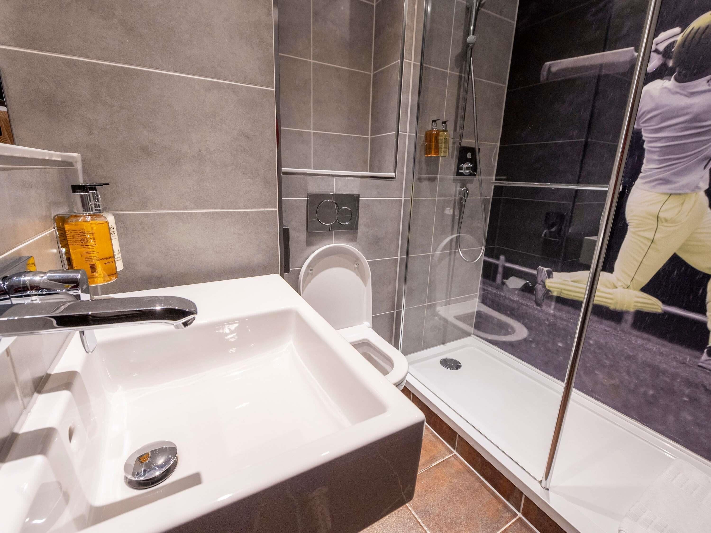 Et moderne badeværelse med en hvid vask, en glasbrusekabine og et toilet.