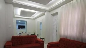 A living room with two red sofas, a white ceiling, and a window with white curtains.