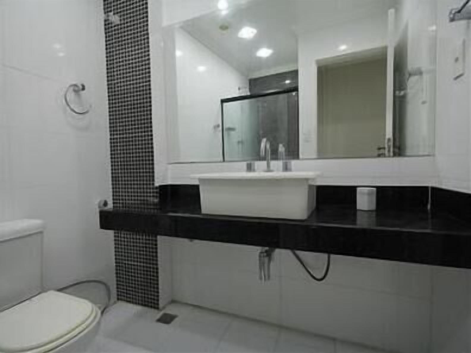 A modern bathroom with a white toilet, a black and white checkered shower area, and a large mirror above a white sink with a black countertop.