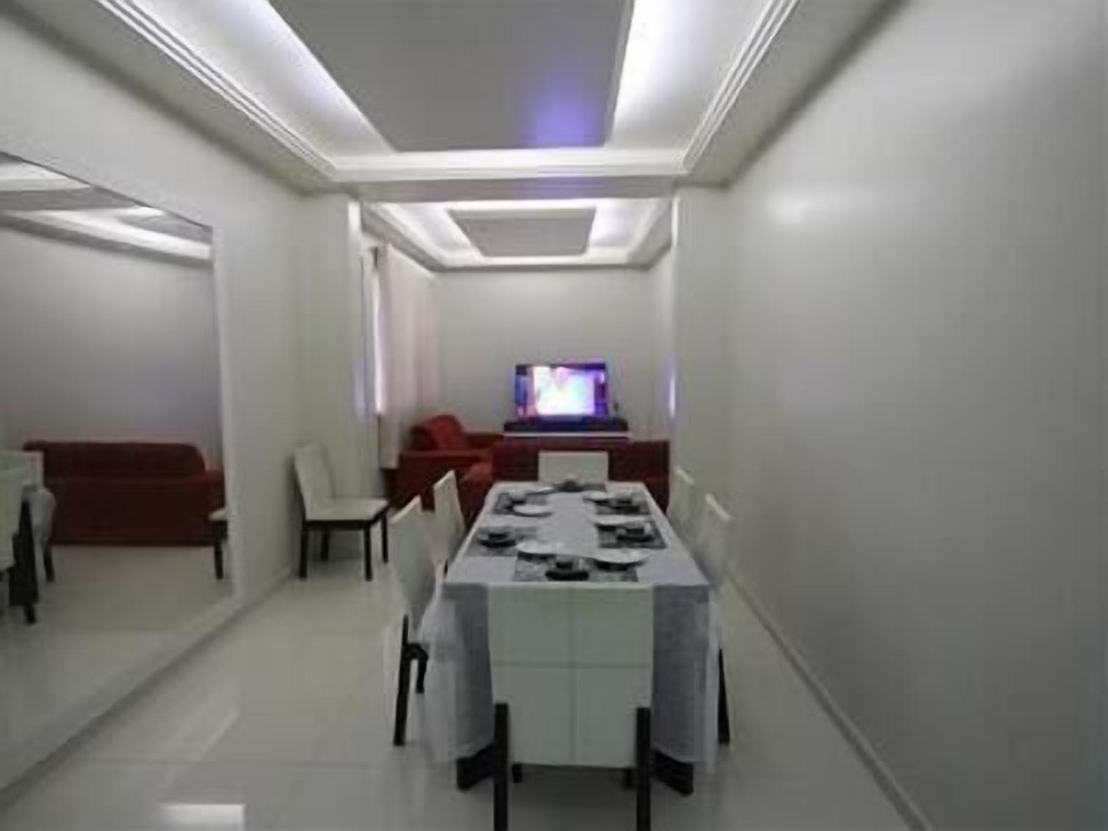 A modern, well-lit room with a dining table set for four, a television in the background, and a red couch.