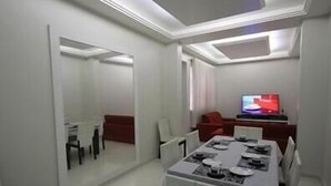 A modern dining area with a white table set for four, a red sofa, and a television in the background.
