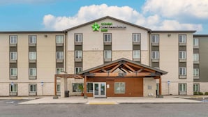 Un hotel StayAmerica con una fachada moderna, varios pisos y una entrada central con un toldo de madera.