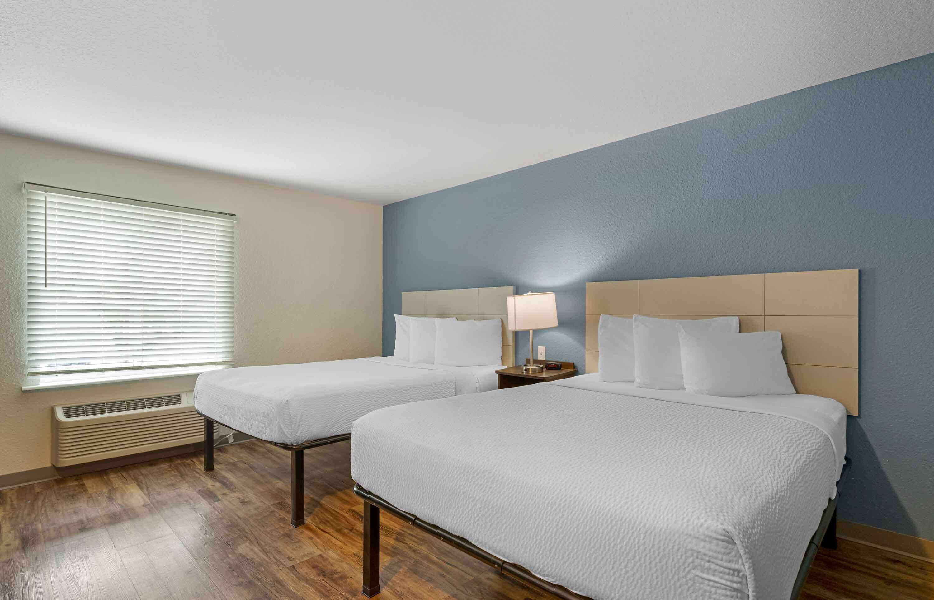 Une chambre d’hôtel avec deux lits, une fenêtre avec des stores, un radiateur et une table de chevet avec une lampe.