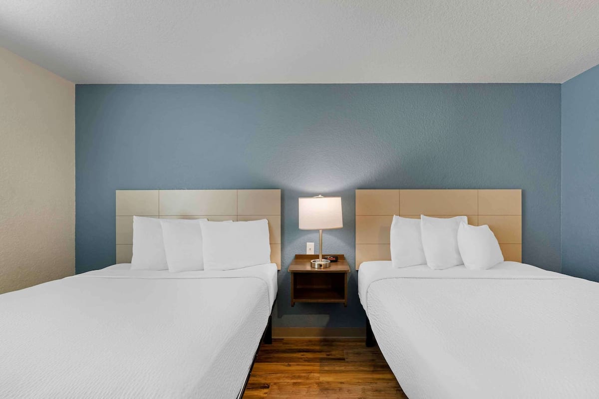 Une chambre d’hôtel avec deux lits, une table de chevet avec une lampe et un mur bleu.