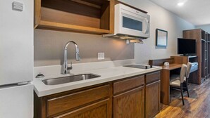 Una cocina compacta con microondas, lavamanos doble y armarios de madera.