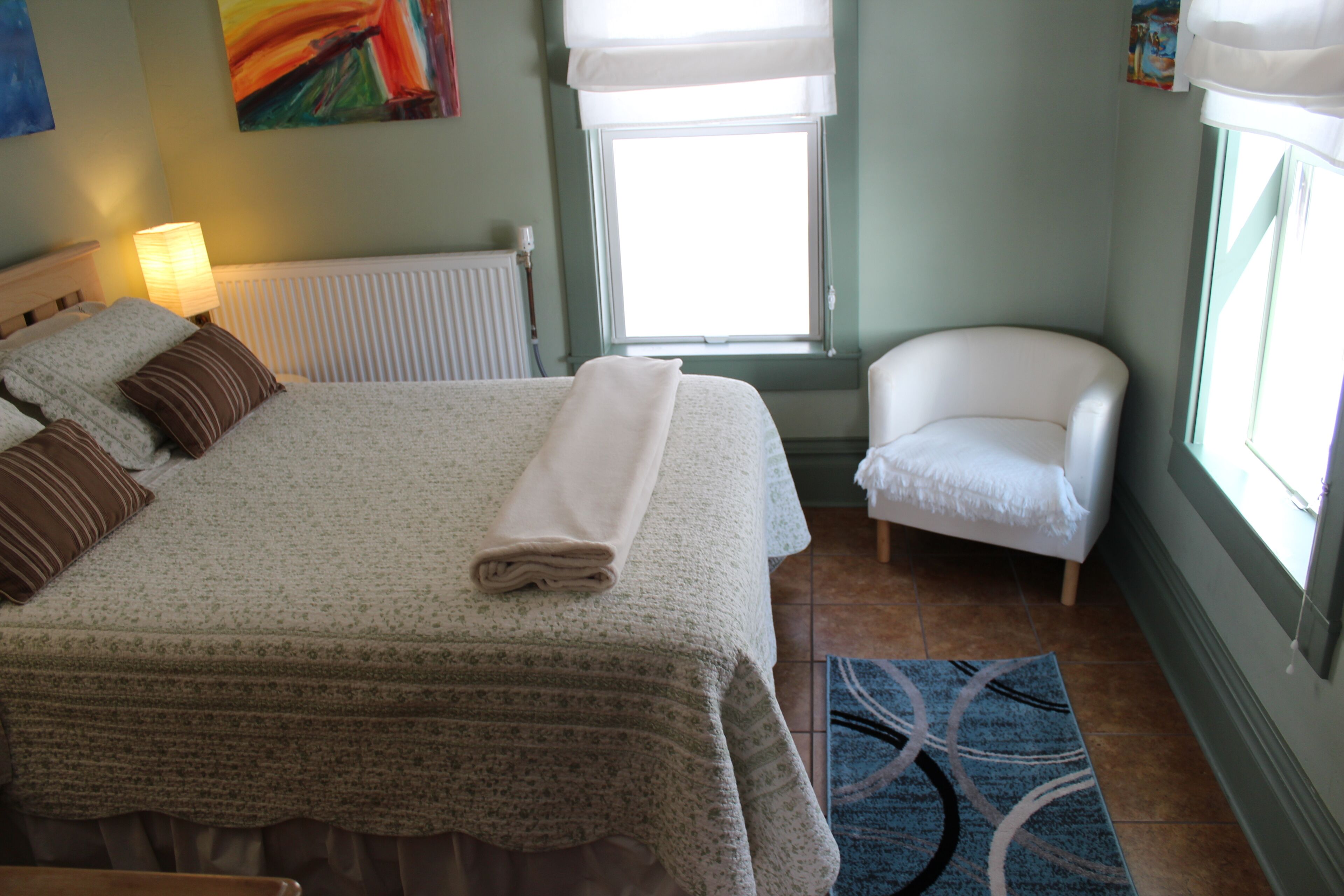 Un dormitorio con una cama grande, una silla, un radiador y una ventana con cortinas.