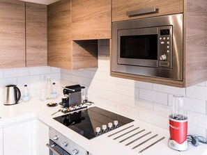 A modern kitchen with wooden cabinets, a stainless steel microwave, a black induction cooktop, and a red blender.