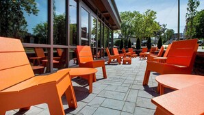 An outdoor seating area with orange chairs and tables, large windows, and a paved floor. - The Hayes Street Hotel, Trademark Collection by Wyndham (Nashville)